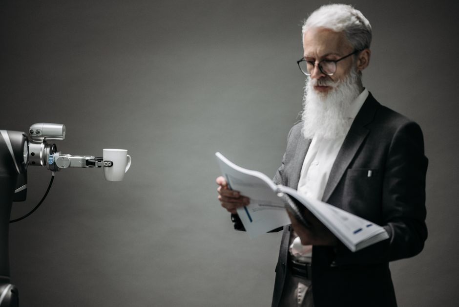 A robot arm assists a professional with a book and coffee in a modern office setup. Technology meets innovation.